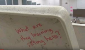 Writing on the back of a classroom chair: "What are they learning sitting here?"