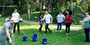 adults playing a team building game outdoors with buckets and rope
