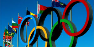 Olympic rings, and array of flags against a blue sky