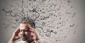 man stressed out, holding head, in front of a whiteboard with tons of scribbles coming from his head