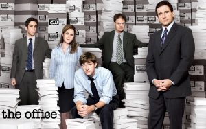 The Office cast, sitting among piles of paper