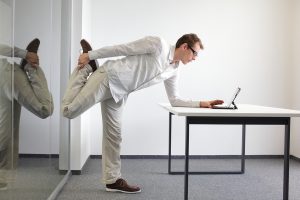 man stretching at his desk, while working on tablet