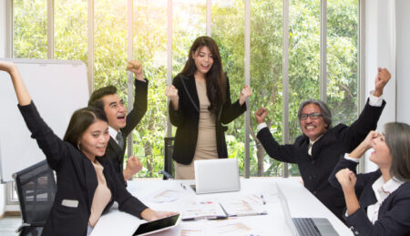 Diverse group of office colleagues at a table, cheering