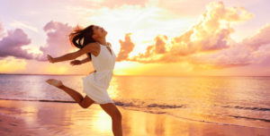 Happy woman running barefoot on sand with sunset in the background