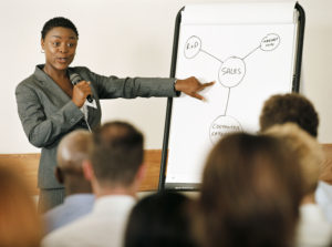 Woman with mic pointing to flip chart